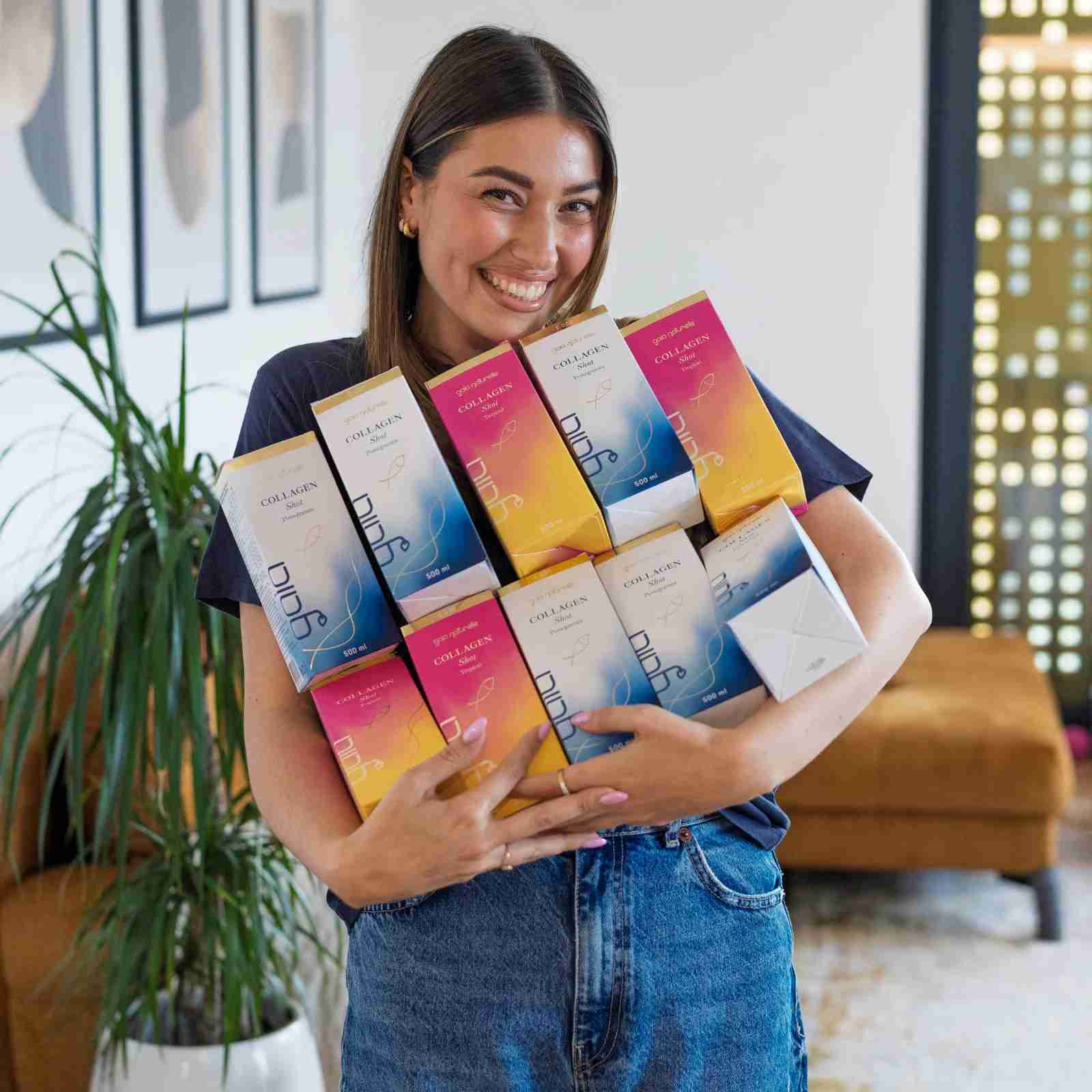Nasmejana mlada ženska drži v rokach več paketov kolagena od Gaia Naturelle.