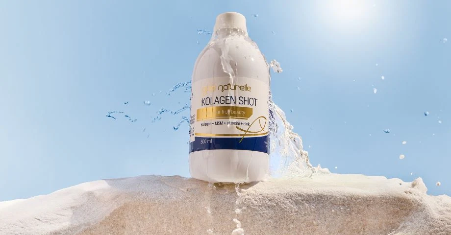 Steklenička Gaia Naturelle Kolagen Shot stoji in kamnu in jo obliva voda, v ozadju sije sonce.